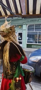 A person stood looking across the road, wearing an outfit for the Krampus Run, and holding a drum
