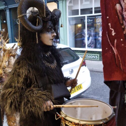 d52f023c-65fa-4cc2-8f1e-9be3c5d91892 A person wearing traditional Krampus outfit for the Krampus Run banging a drum